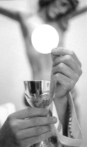 Kapłan unosi konsekrowaną hostię nad kielichem podczas Eucharystii.